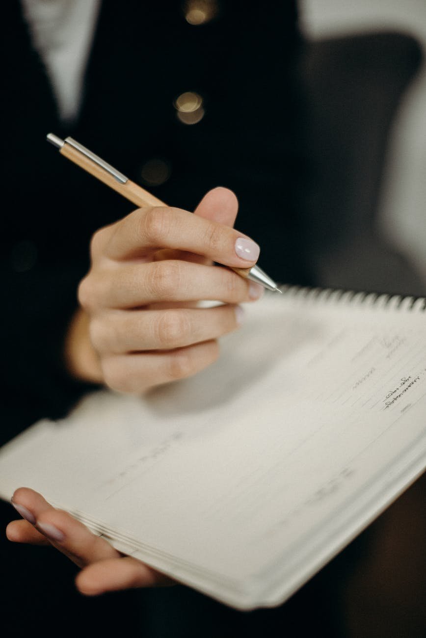 closeup of hand of a person holding orange click pen writing on notebook